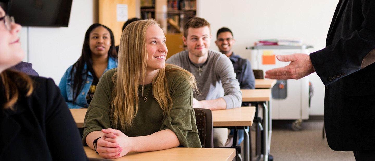 classroom full of students watching a professor who is gesturing with his hands